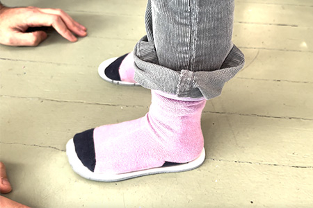 A child standing on a pair of her shoe insoles to visualize if she has growing room inside her shoes.