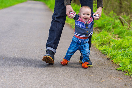 A father holding his baby who is learning how to walk with a pair of first walking shoes.