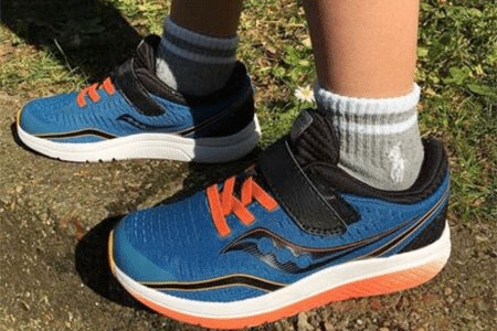 A boy wearing a pair of blue and orange Saucony shoes.
