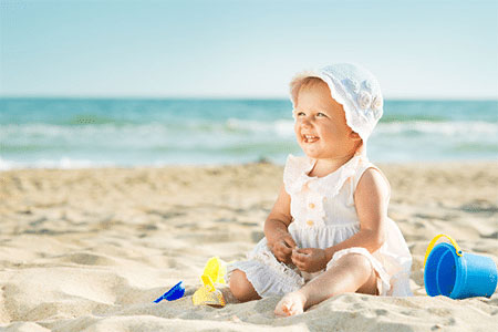 Toddler girl sitting on the beach waiting to wear a pair of water shoes.