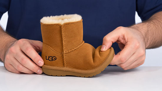 Hands bending the front of a toddler UGG boot to demonstrate its flexible sole and how it bends at the toes.