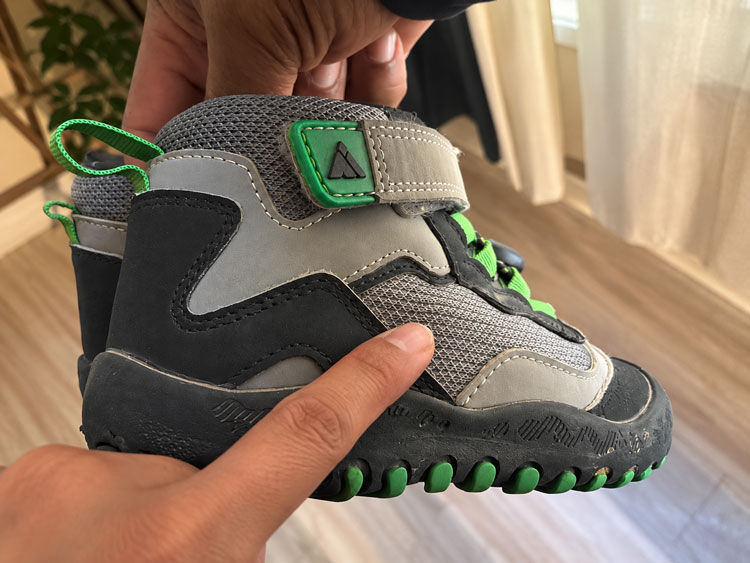 Close-up of a children's outdoor boot with a hand pointing to the breathable mesh fabric on the side of the shoe.